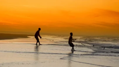 Garotos manuseiam rede de pesca nas praias de Moçambique, com sol se pondo ao fundo, alaranjado.